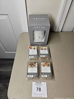 Fragrance melt warmer in grey Trapp Fragrances box with four unopened wax melt packs arranged in front on a table.