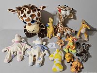 Photo showing the entire collection of 11 giraffe themed plush toys and two cow-like plush toys arranged on a flat surface.