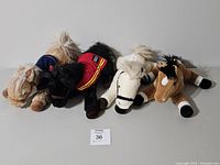 Four plush horse toys arranged side by side: beige, black, white, and tan colors visible