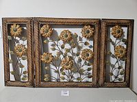 Full view of the three-panel metal flower wall art laid flat showing sunflower designs and textured frames.
