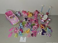 Wide view showing 20 My Little Pony toy ponies, pink car toy, plastic combs, and other pony accessories arranged on a flat surface