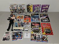 Photo showing entire Nascar items lot including Funko POP figures, die-cast cars, trading cards, driver figurine, and the tow truck models all arranged on a surface.