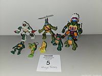 All 9 Ninja Turtle figures and toys arranged on a white surface showing variety in design and size