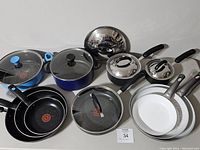 Overview of all pots, pans, lids, and mixing bowls arranged on a white surface showing assortment and condition