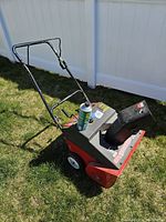 Full side view of the used MTD Yard Machines snowblower with bent handle sitting on grass near white fence