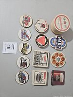 Top view of a stack of round and square vintage drink coasters with automobile illustrations and beer brand logos spread around.