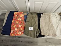 Seven pairs of women's shorts arranged side by side with various colors including navy, floral orange, olive, black, and khaki visible.