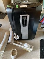 Full view of black Haier portable air conditioner with vent hoses and attachments on the floor next to it.