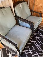 Two large metal framed patio chairs with light blue padded cushions, angled view showing both chairs side by side on a patterned rug.