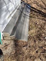 A stack of grey composite decking boards leaning against an exterior wall, showing multiple planks and profile.