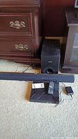 Philips CSS2123B/F7 sound bar and subwoofer with remote and power adapter sitting on carpeted floor.