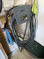 Yardworks garden hose coiled on gray plastic hose hanger with nozzle attached, sitting on green mat near wall.