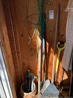 Photo showing garden tools including a shovel, fork, rake, sprinkler, and a decorative pot inside a wooden shed.