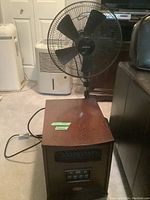 Full view showing Truman infrared heater in wood finish and black Sunbeam oscillating fan behind it.