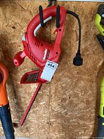 Front side view of a red Homelite hedge trimmer with power cord and blade guard.