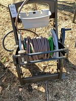 Front view of the brown plastic hose reel with garden hose coiled and white storage container on top, showing handle and wheels.