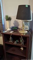 Lamp with black shade and metal genie lamp style base, Sony digital clock radio, small urn-like vase with faux succulent on wood shelf
