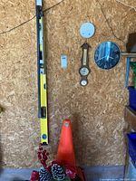 Full view of lot showing yellow levels, orange cone, decorative planter, wall clock and barometer on plywood wall