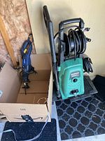 Greenworks pressure washer with hose and wand next to the Mastercraft reciprocating saw in a cardboard box.