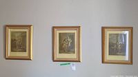 Three framed prints hanging on a wall with gold-colored frames showing historical street scenes