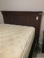 Wooden headboard attached to bed frame with mattress on top, dark brown finish, simple design.