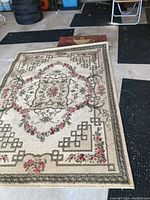 Photo showing large floral pattern rug alongside black rubber backed runners and smaller mats on concrete floor.