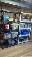 Two resin shelving units side by side with assorted plastic containers and household items on shelves, but contents are not included in lot.