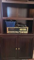 Technics stereo cassette deck model 630T placed in a wooden cabinet with cables and a blue storage basket on top.
