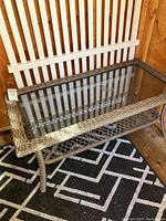 Patio table and white vinyl fence panel shown together inside wooden shed space on black and white patterned rug.