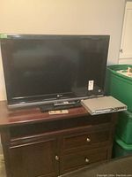 Front view of Sony Bravia TV on stand with Koss DVD player and remotes placed on wooden furniture.