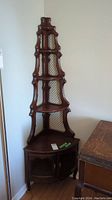 Full view of wooden corner shelf showing cascading design and two door cabinet base with metal wire lattice.