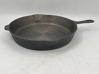 Side angle of vintage cast iron skillet showing shape, handle, and pouring spouts with surface wear.