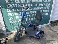 Blue electric tricycle with front basket, seat with backrest, and three wheels shown from side.