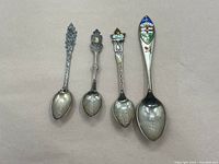 Four sterling silver collector's spoons laid side by side showing overall size and design.