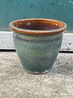 Front angle of the vintage glazed green ceramic planter pot with a brown rim showing drip-style glaze and wear at the base.