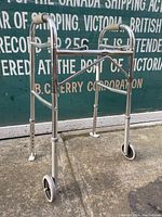 Front angled view of the walker showing chrome metal tubing, front wheels, rubber tipped rear legs, and adjustability.