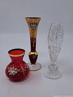 Photo showing the three vintage glass vases together. Ruby red vase is squat with floral and gold detail, maroon vase is slender with gold and floral, clear vase is etched and cut glass.
