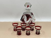 Full view of the decanter with stopper and six glasses arranged in front showing red geometric cut design.