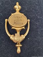 Top view of brass door knocker showing the inscription and Claddagh design on black fabric background.