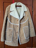 Front view of the tan suede jacket showing shearling collar, pocket trim, buttons, and John Deere patch logo on left chest.