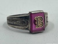 Close-up side view of the vintage silver ring showing the purple stone and gold letter "B" on top, with textured band details.