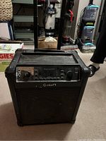 Front view of Ion Block Rocker speaker showing control panel, handle, and wheels, placed indoors on carpet.