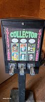 Front view of the coin-operated vintage card vending machine called 'The Collector' with three metal levers for dispensing cards and colorful card images on front panel.