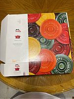 Closed Staub branded box featuring colorful ceramic lid prints, showing brand and country of origin (France).