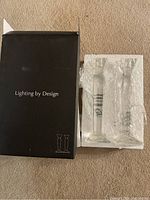 Photo shows two clear crystal candleholders wrapped in protective packaging next to original box labeled 'Lighting by Design'.