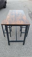 Rectangular dining table with wood top and black metal legs photographed from an end angle showing full table length and surface details.