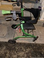 Side view showing green frame, padded handles with brake levers, and fabric seat with backrest.