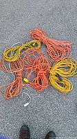Photo of five used extension cords coiled and placed on pavement; cords are orange, yellow, and white colors.