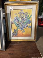 Framed purple iris flower picture in gold ornate frame with cream matting, on wood floor.