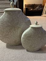 Two lidded ceramic vases on carpet floor with dark furniture background